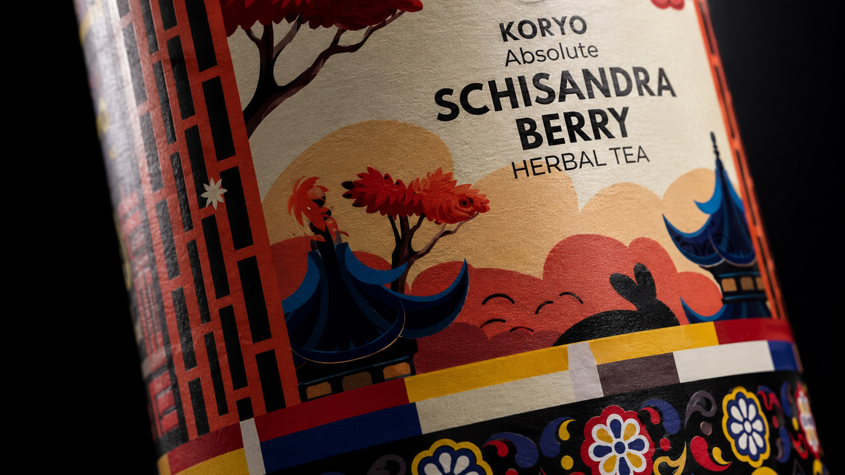 Close view of the KORYO Schisandra Berry Herbal Tea label featuring product typography, Korean-inspired architecture, red trees, layered landscape forms, rabbit silhouette, and ornamental borders.