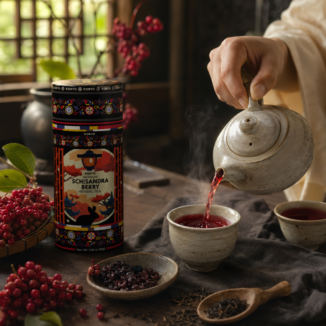 A person pours red herbal tea beside KORYO Schisandra Berry Herbal Tea packaging, fresh berries, dried ingredients, ceramic cups, and a teapot.