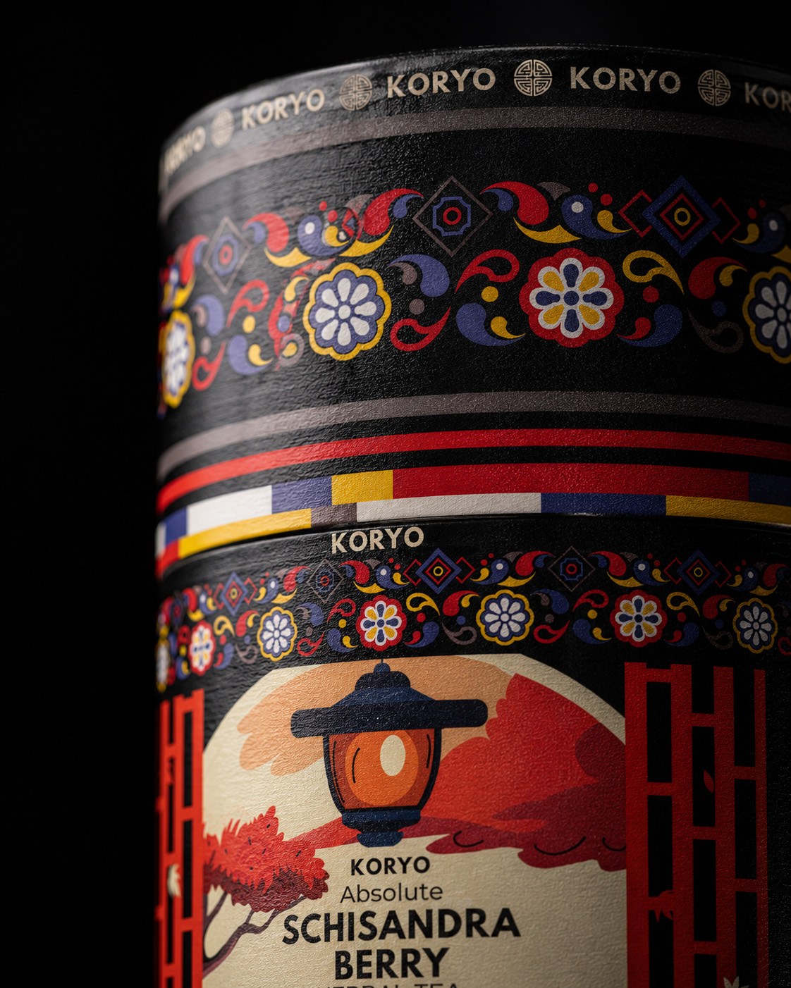 Macro view of the KORYO Schisandra Berry Herbal Tea canister showing the branded upper rim, Korean-inspired floral ornament, multicolor bands, curved surface, and textured print.
