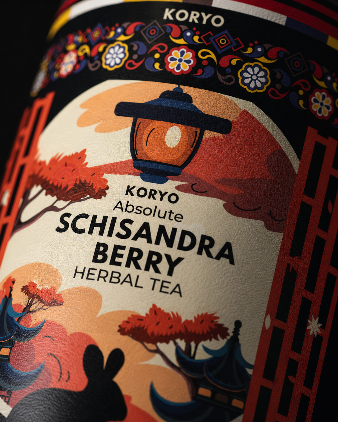 Angled macro view of the KORYO Schisandra Berry Herbal Tea front label showing the lantern, product typography, Korean-inspired illustration, ornament, and curved printed surface.
