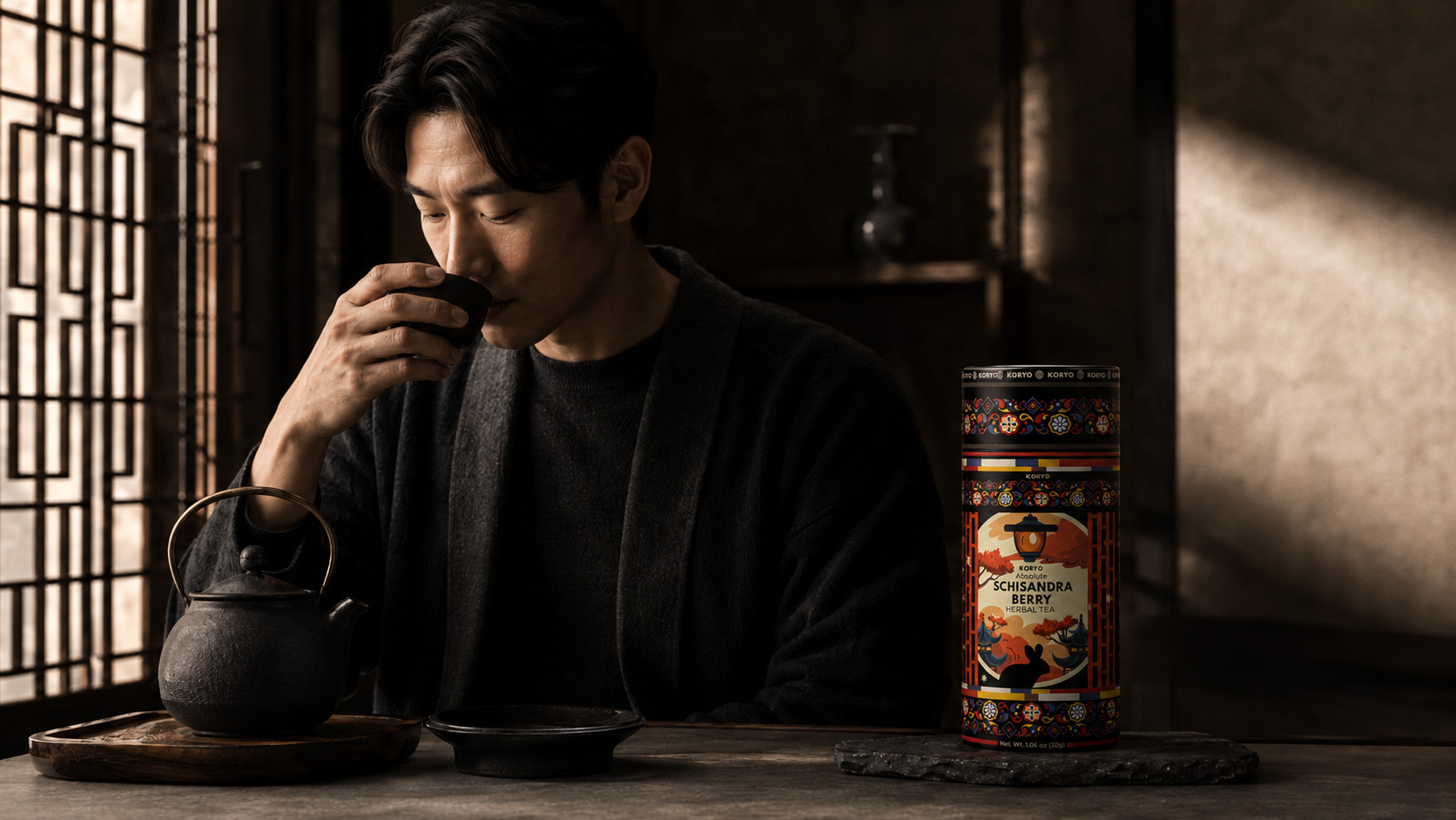 Man drinking tea beside KORYO Schisandra Berry Herbal Tea packaging and dark ceramic teaware in a warm Korean-inspired interior.